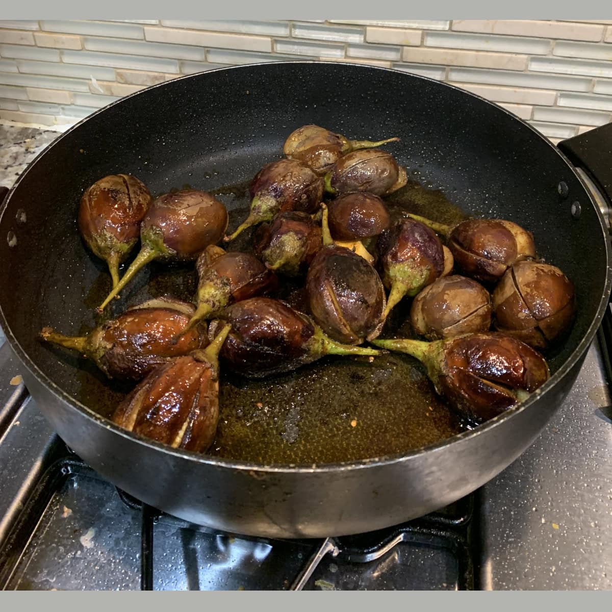 spiced slit eggplant sauteed in a black pan.