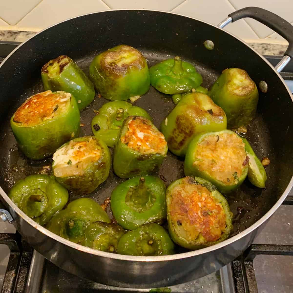 stuffed bell pepper with stalk being cooked in a black pan.