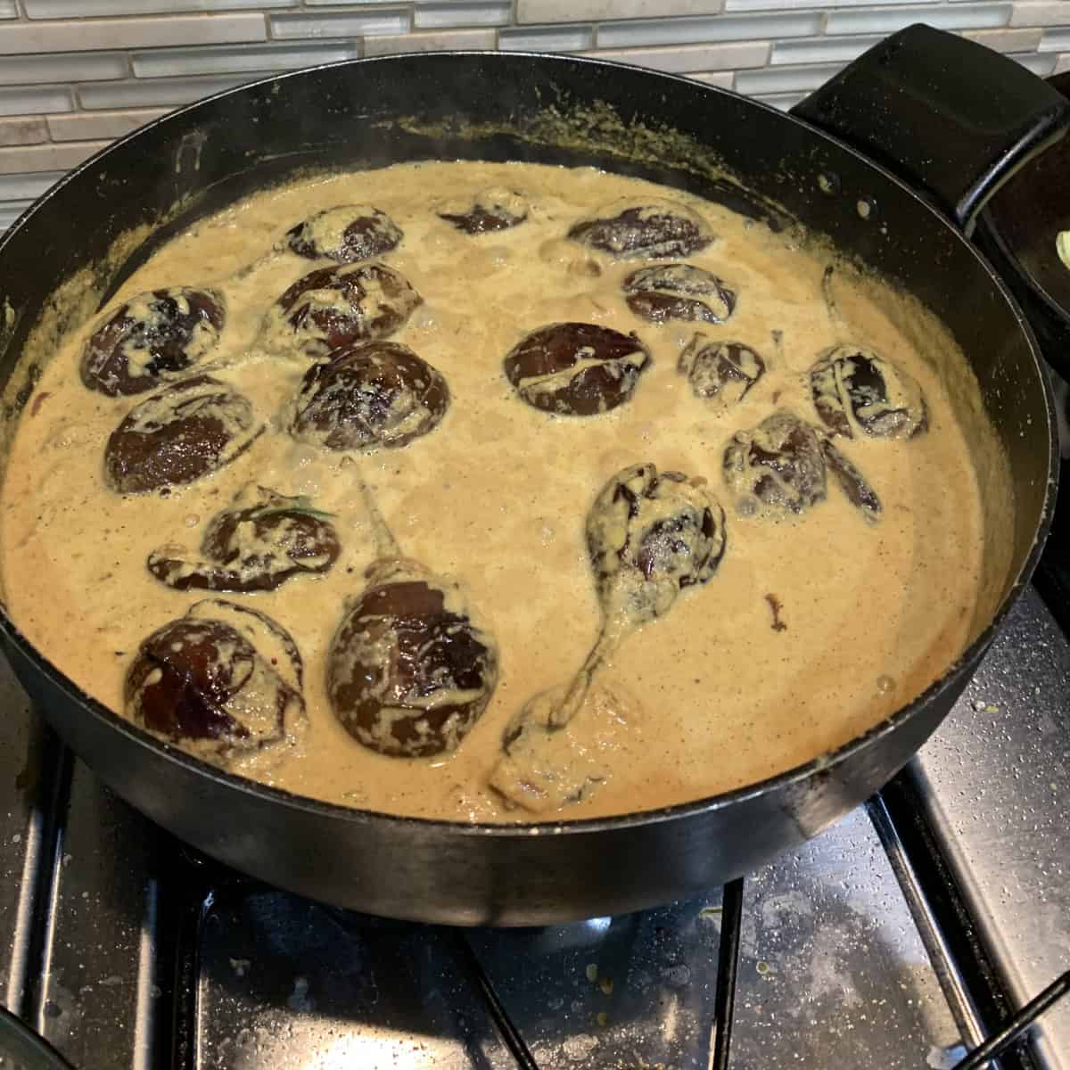 Bagara baingan being cooked in a black pan on stove top.