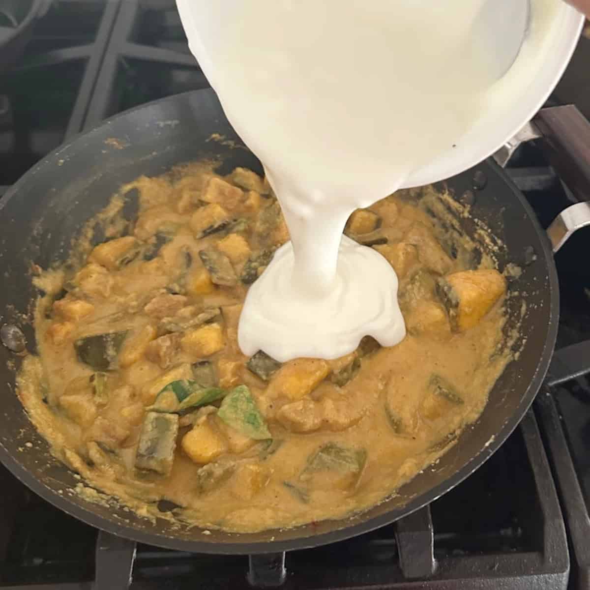 whisked yogurt being added to kaalan in a black pan.