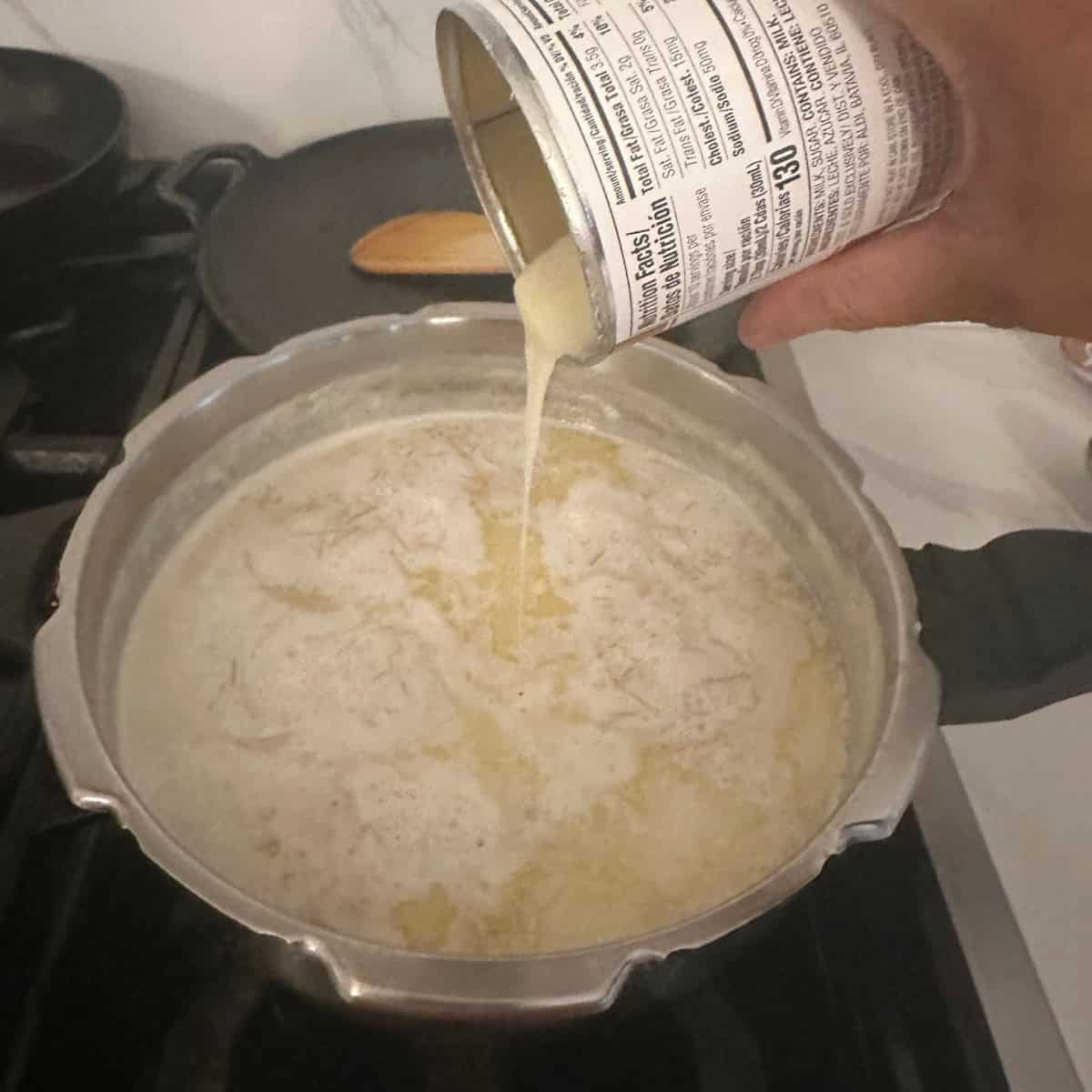 Adding condensed milk to the payasam cooking in a cooker.