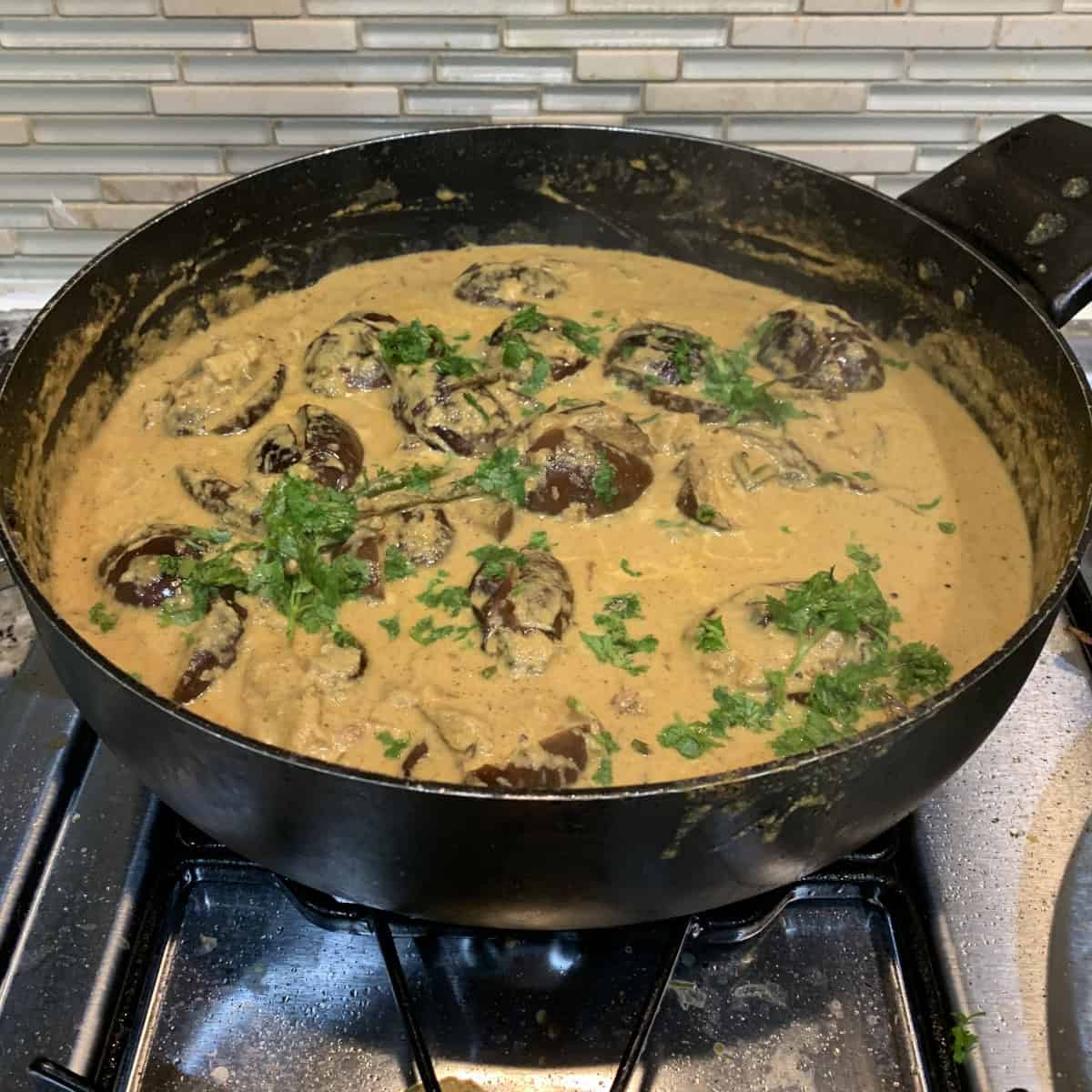 Bagara baingan being cooked in a black pan on stove top.
