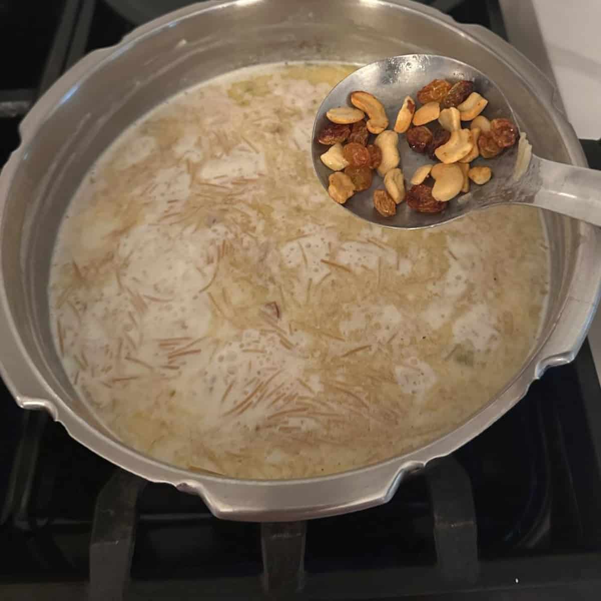 cooking Vemicelli payasam in a pressure cooker and adding in fried nuts and raisins.