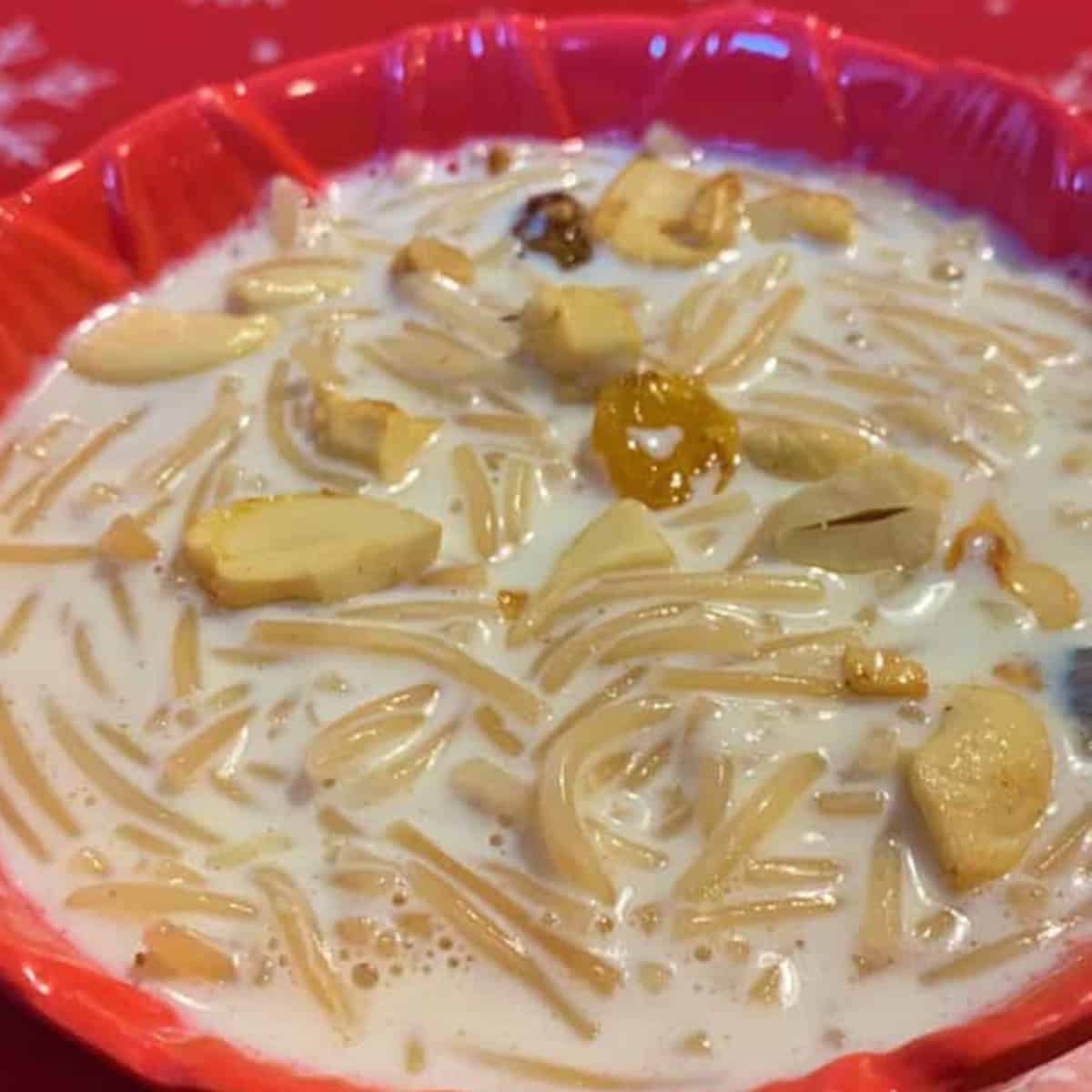 Vermicelli payasam served in a pink bowl topped with fried nuts and raisins.