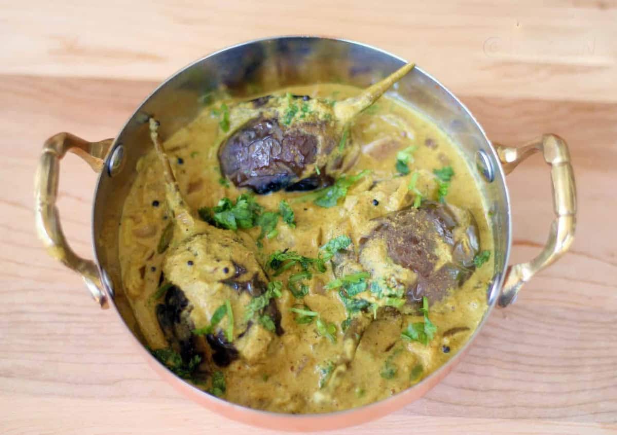 Bagara Baingan served in a copper vessel on a wooden board.