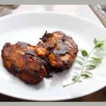 pan fried Tilapia served on a white plate with a stalk of curry leaves on the side.