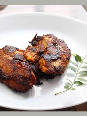 pan fried Tilapia served on a white plate with a stalk of curry leaves on the side.
