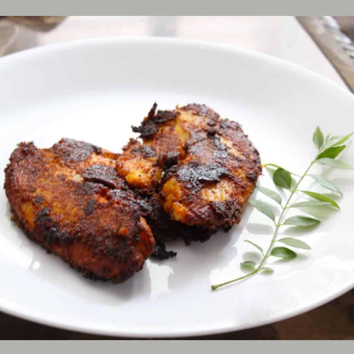 pan fried Tilapia served on a white plate with a stalk of curry leaves on the side.