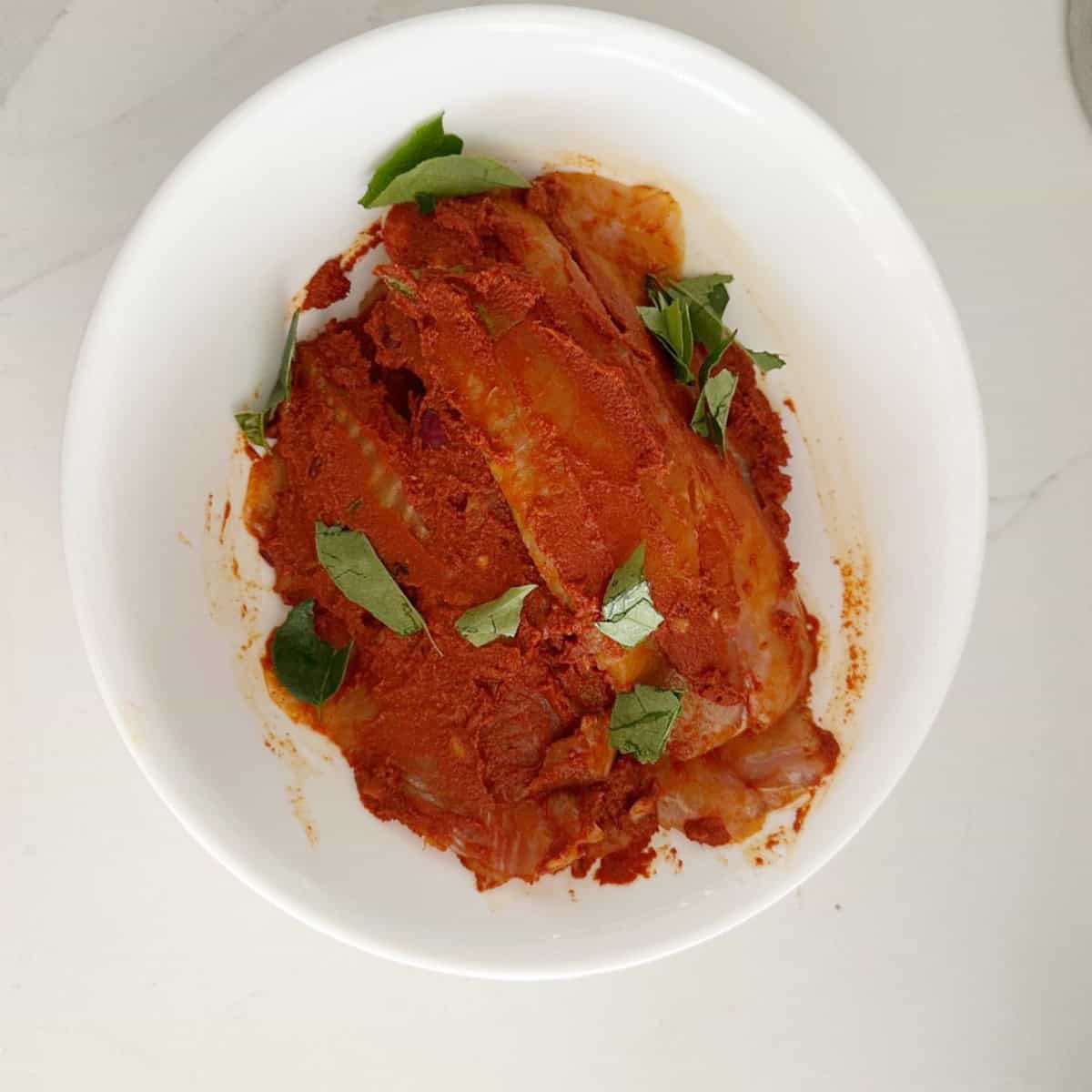 Tialpia coated with marinade in a white bowl.