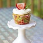 vanilla cupcakes with cream cheese frosting on a white cupcake stand with a strawberry and mint on top.
