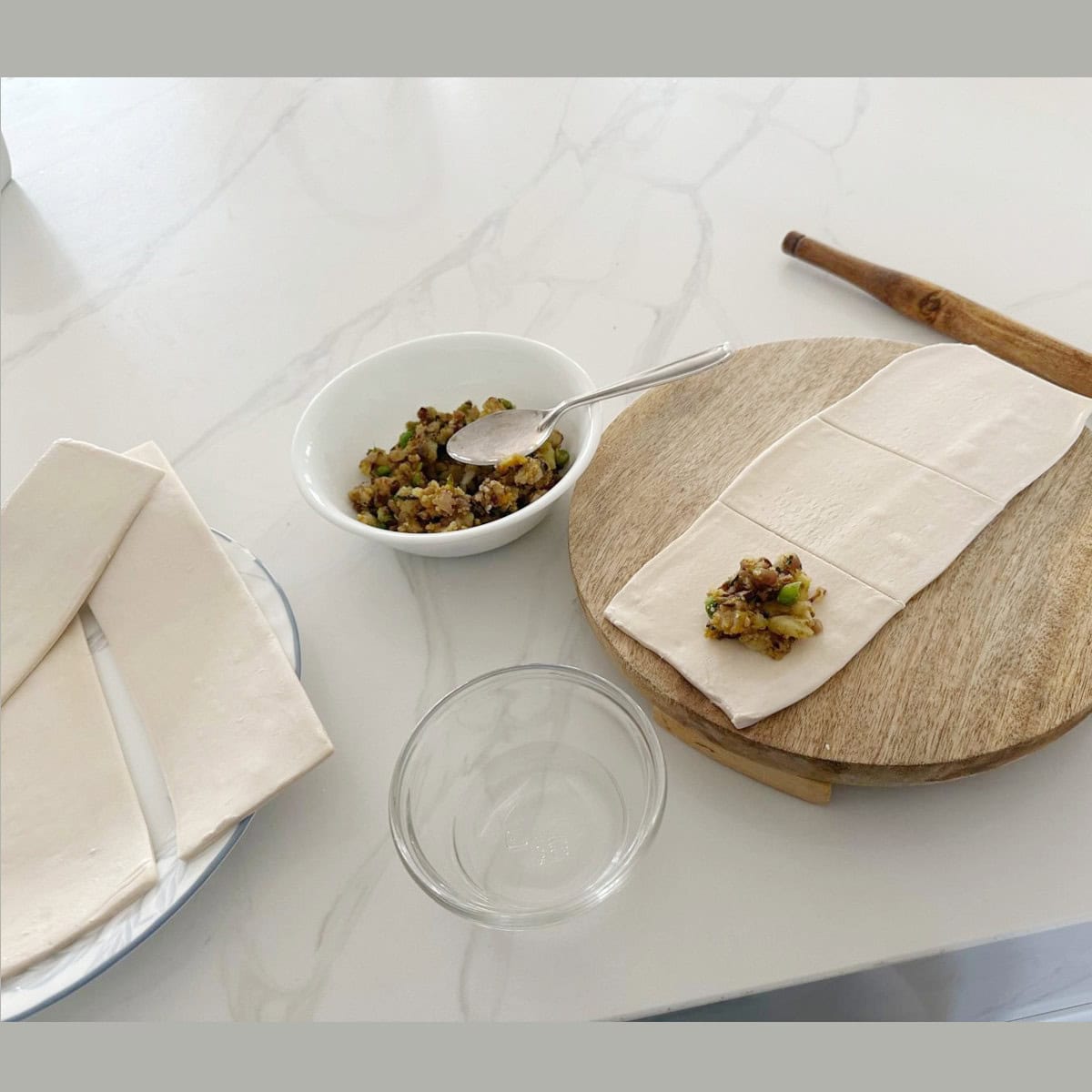 pastry sheets being filled with vegetable filling on a wooden board.