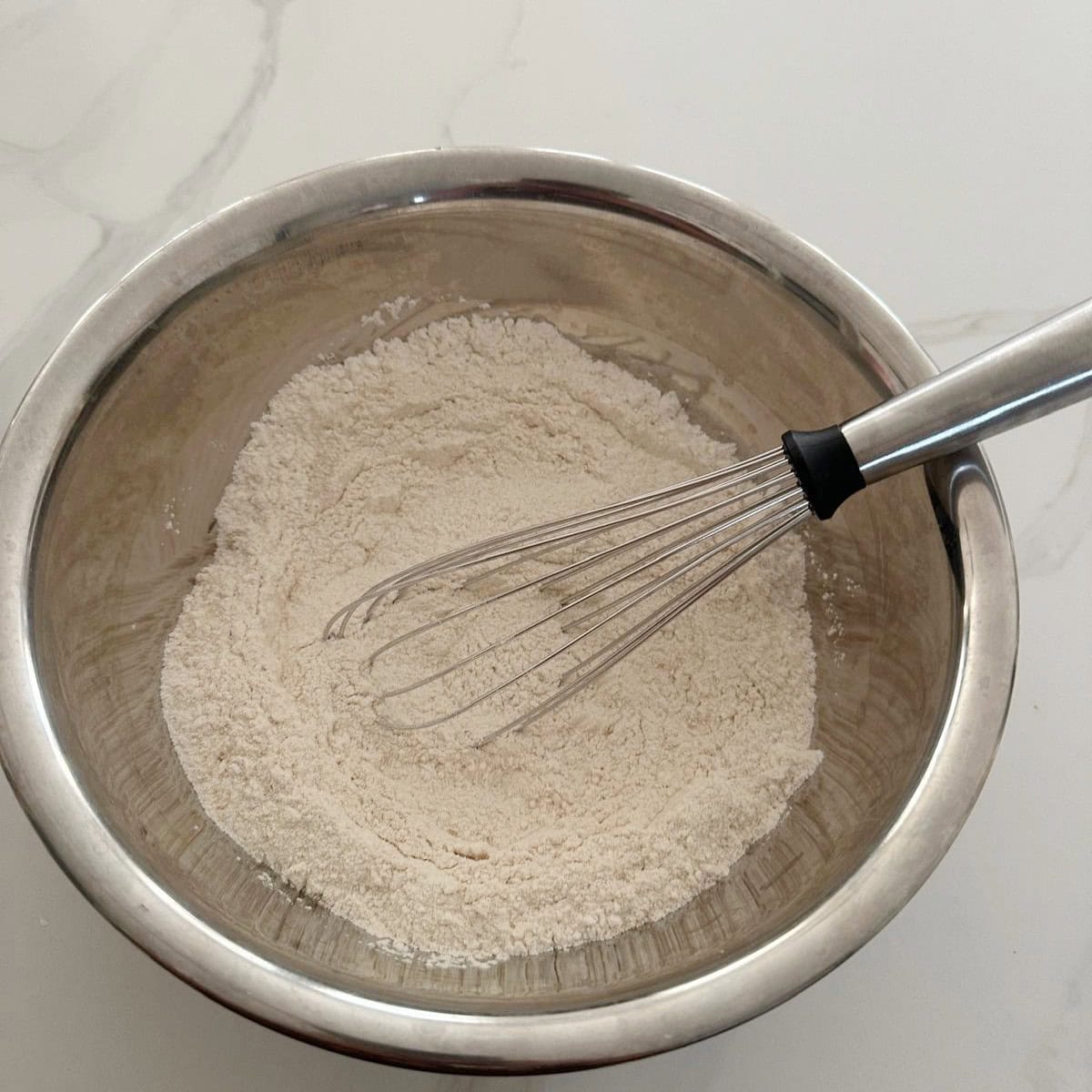 Flours with whisk in a steel bowl to make unniappam.
