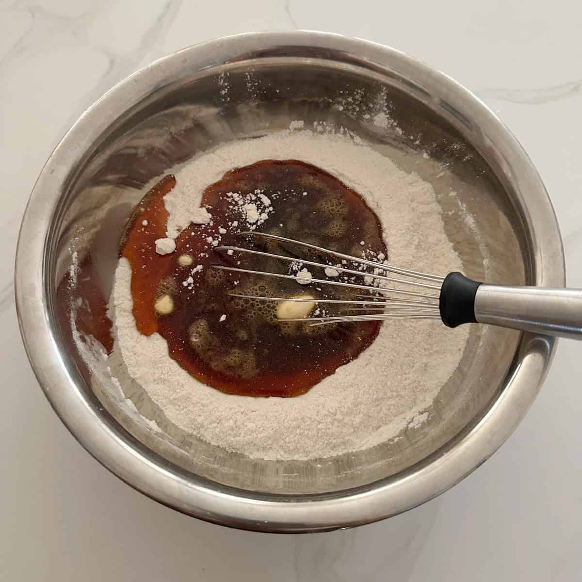 hot jaggery solution added to unniappam batter in a steel bowl with a whisk to mix it.