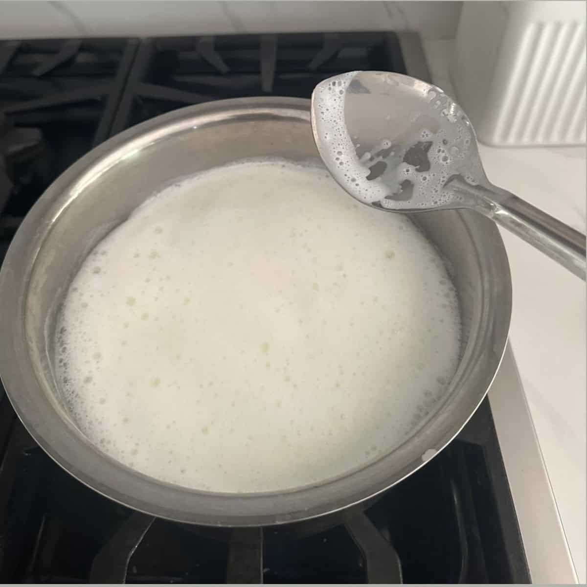 milk boiling in a steel bowl and stirred using a steel spoon.