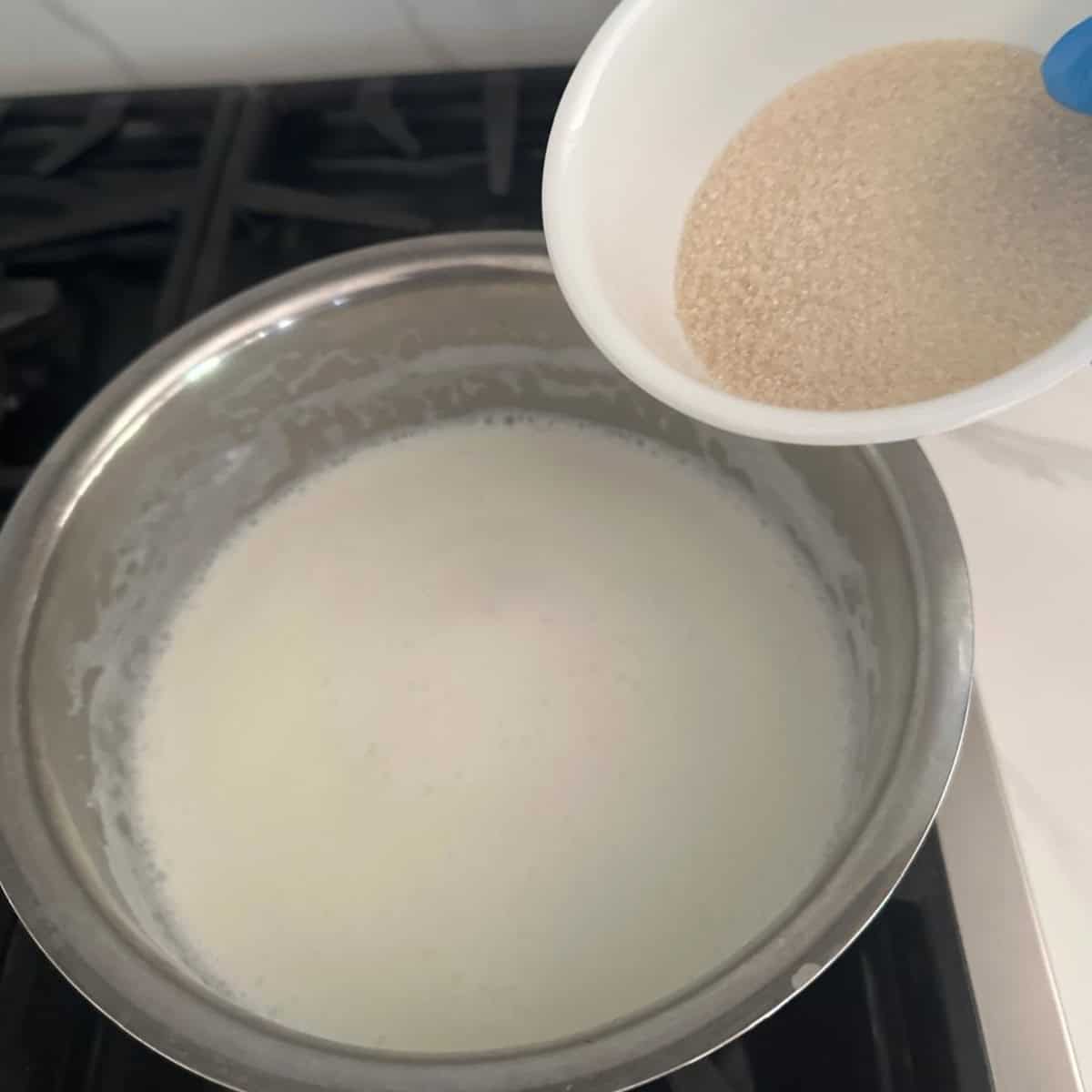 sugar being added to a bowl of steel with boiled milk.