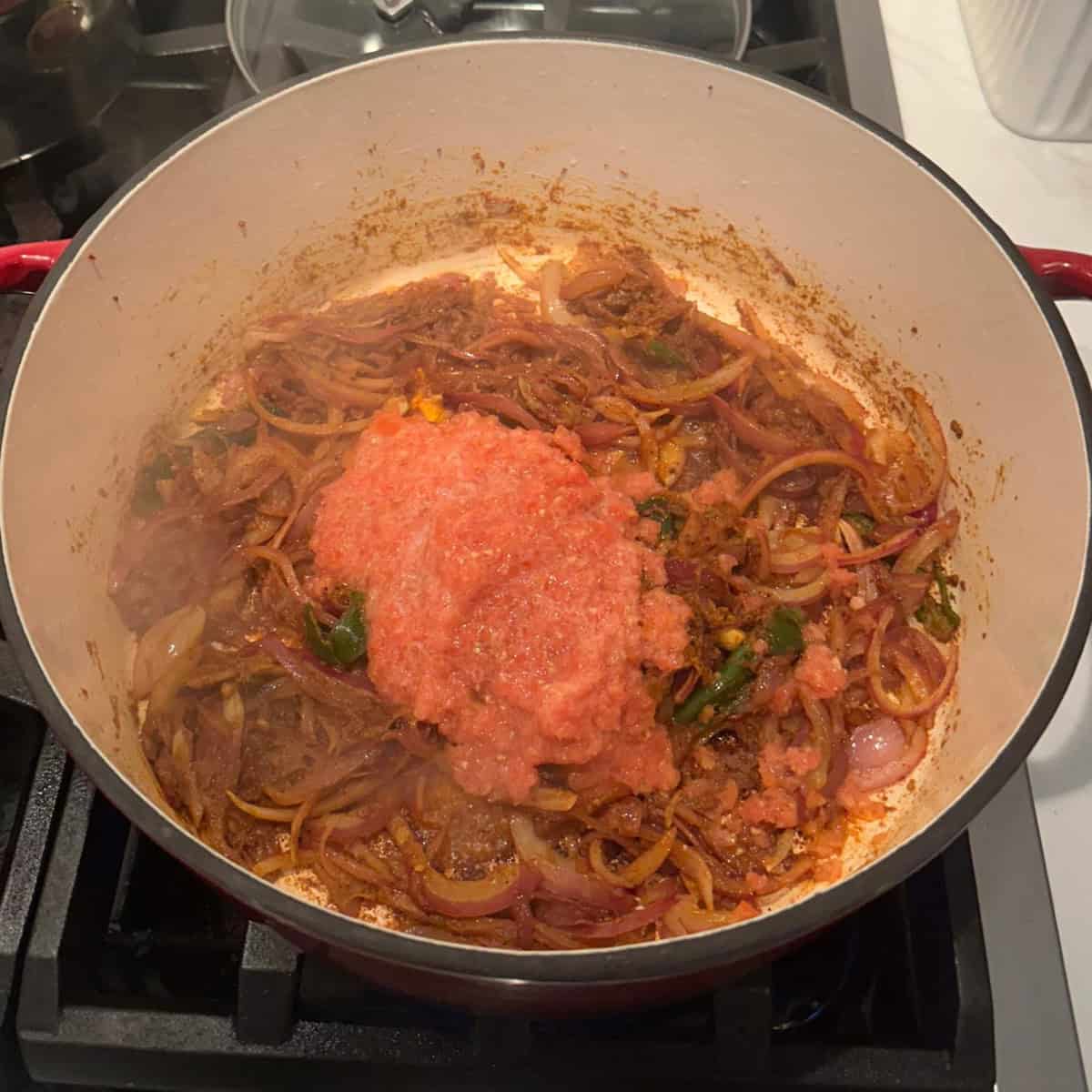 Tomato paste added to the curry in a cast iron pot.