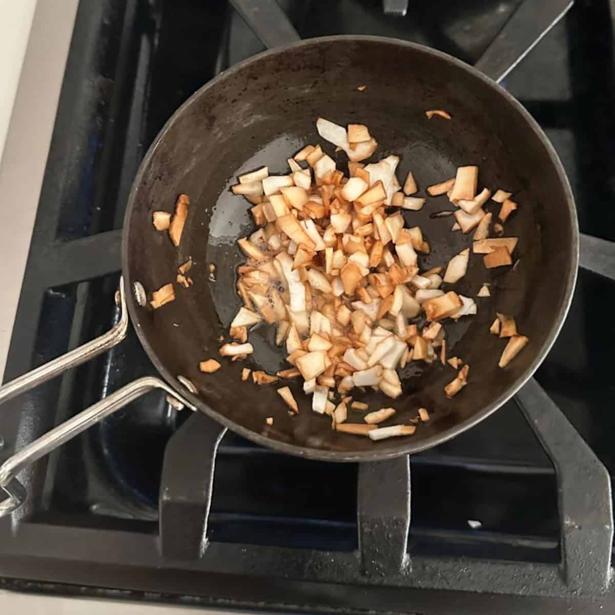 coconut bits being fried in a small black pan.