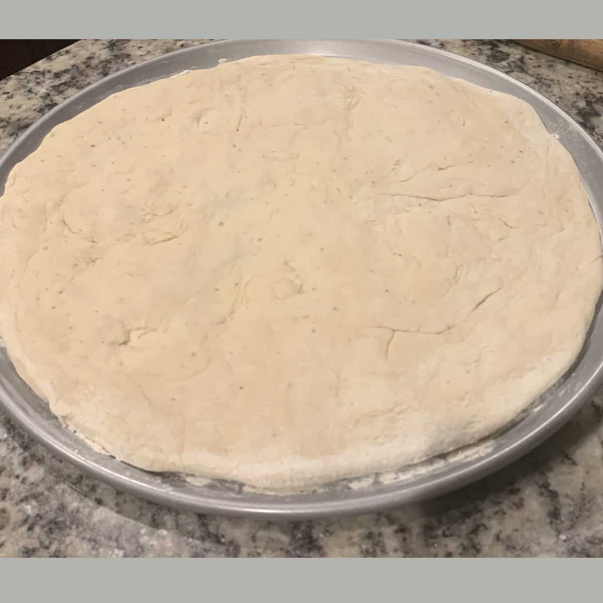 pizza crust rolled out on a silver pizza pan.