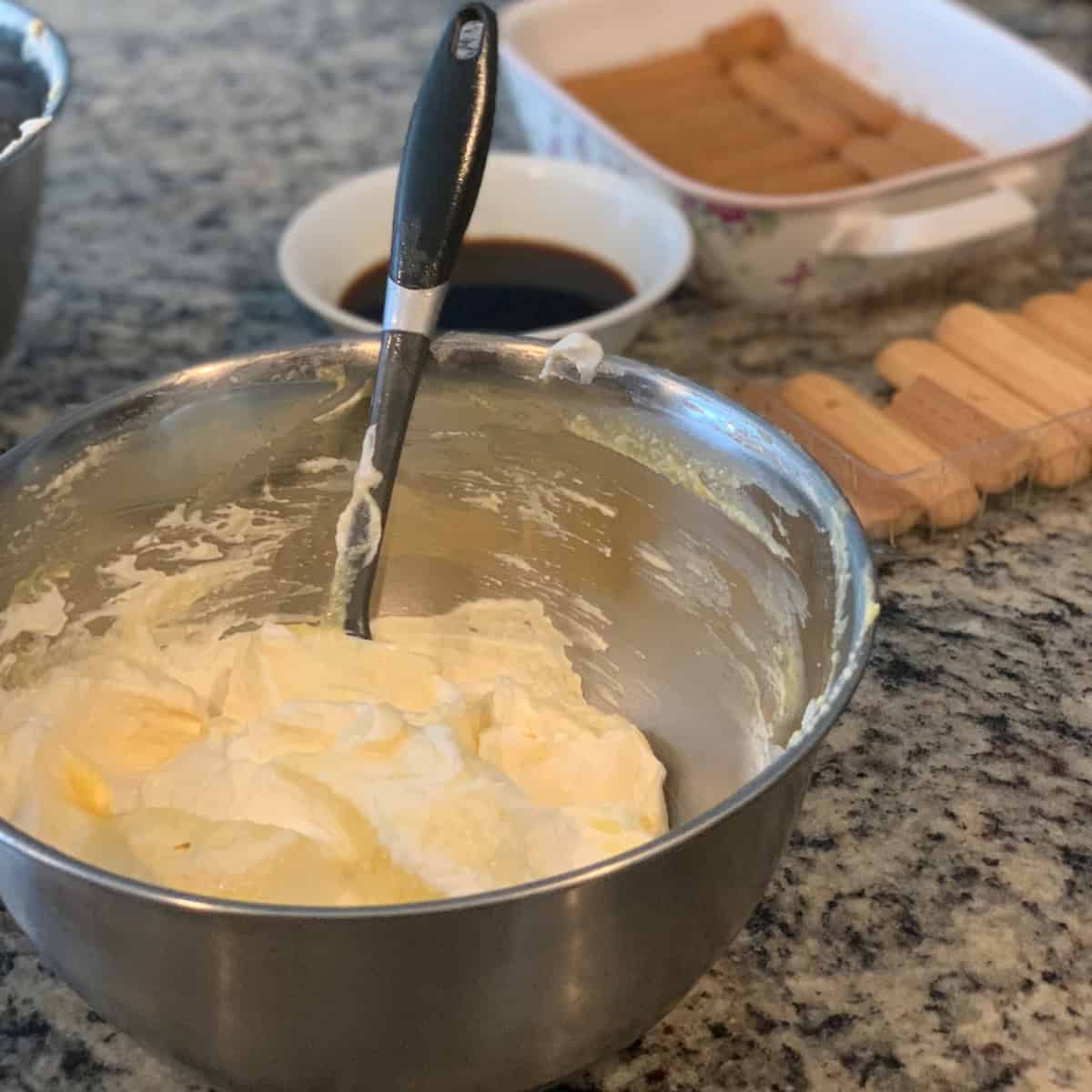 whipped cream with mascarpone and egg with sugar mixed up to make the Tiramisu layers in a steel bowl with a spatula.