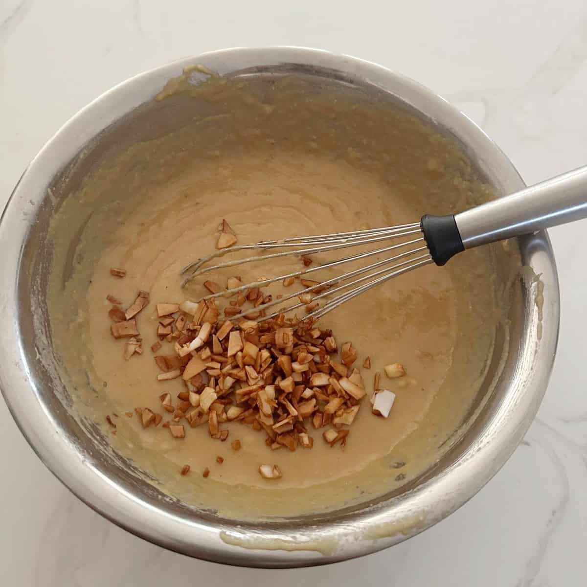 unniappam batter with fried coconut bits added to it and a whisk.