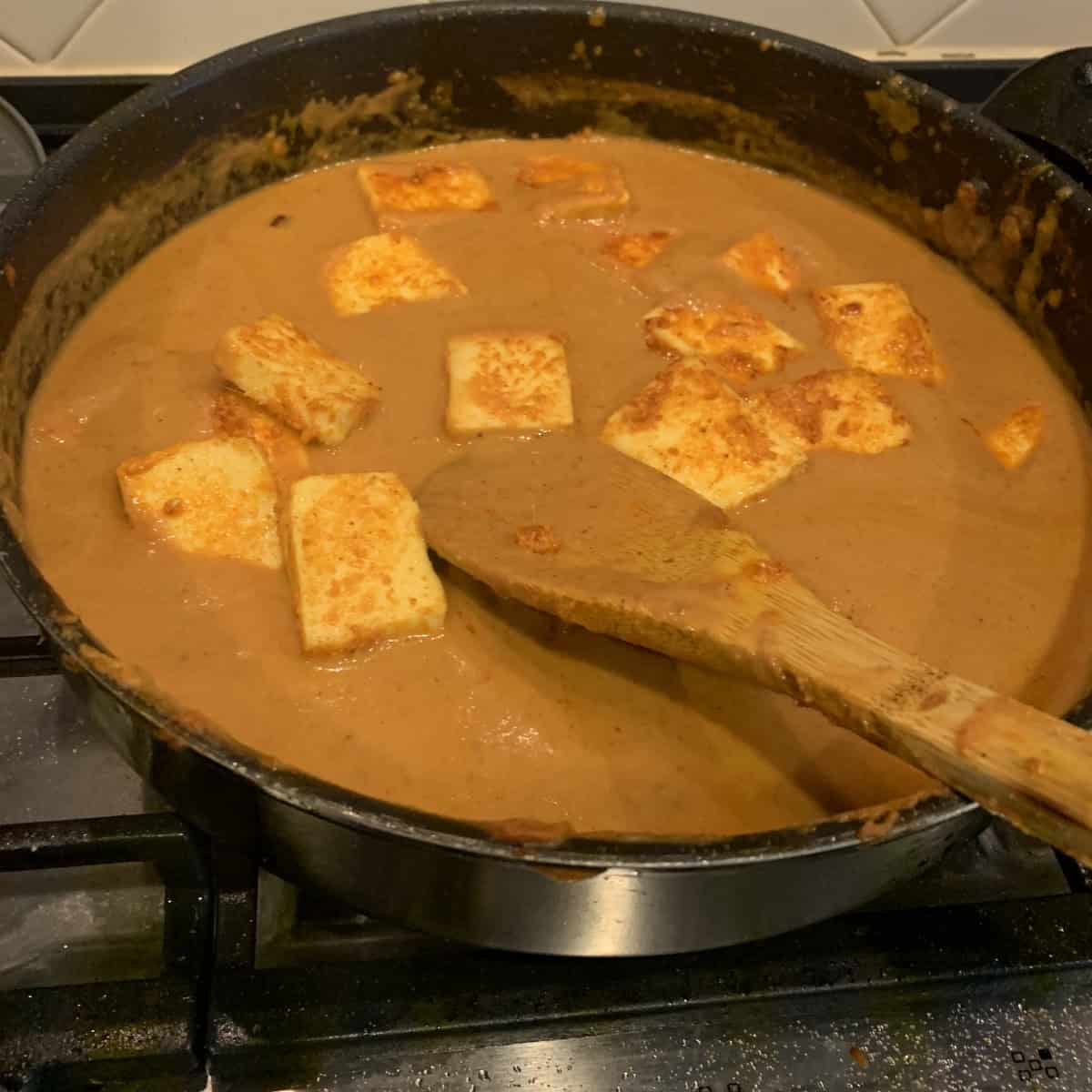 Paneer Tikka Masala being prepared in a black pan with a wooden spoon.