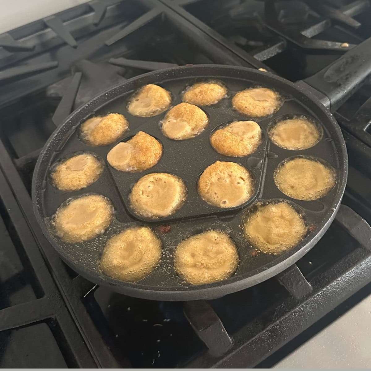 unniappam cooking in an appe pan on a gas stove.