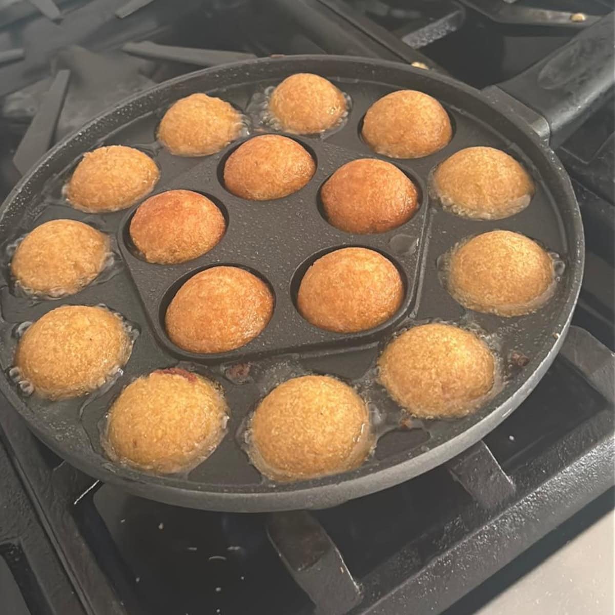 unniappam cooking in an appe pan on a gas stove.