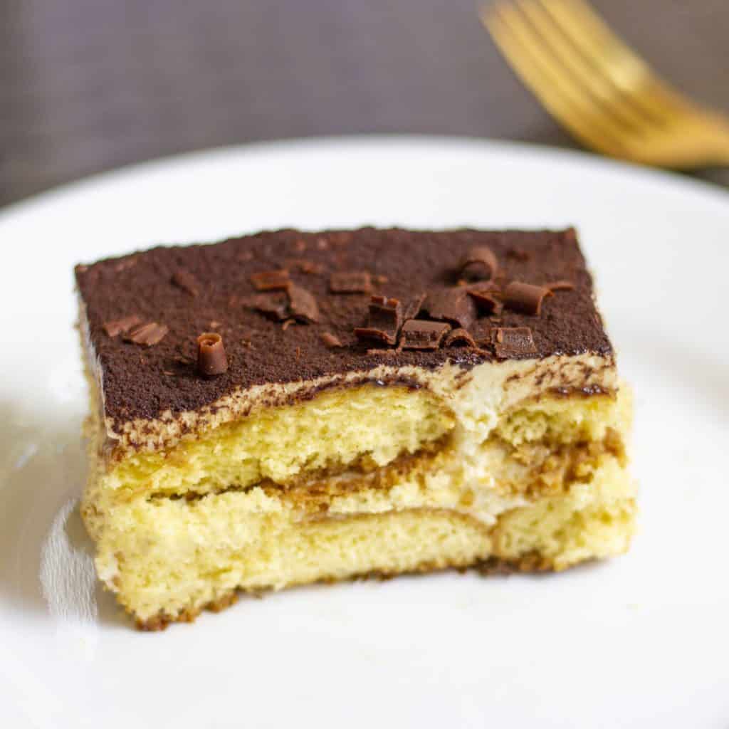 Tiramisu recipe with eggs served in a white dessert plate with a golden fork.