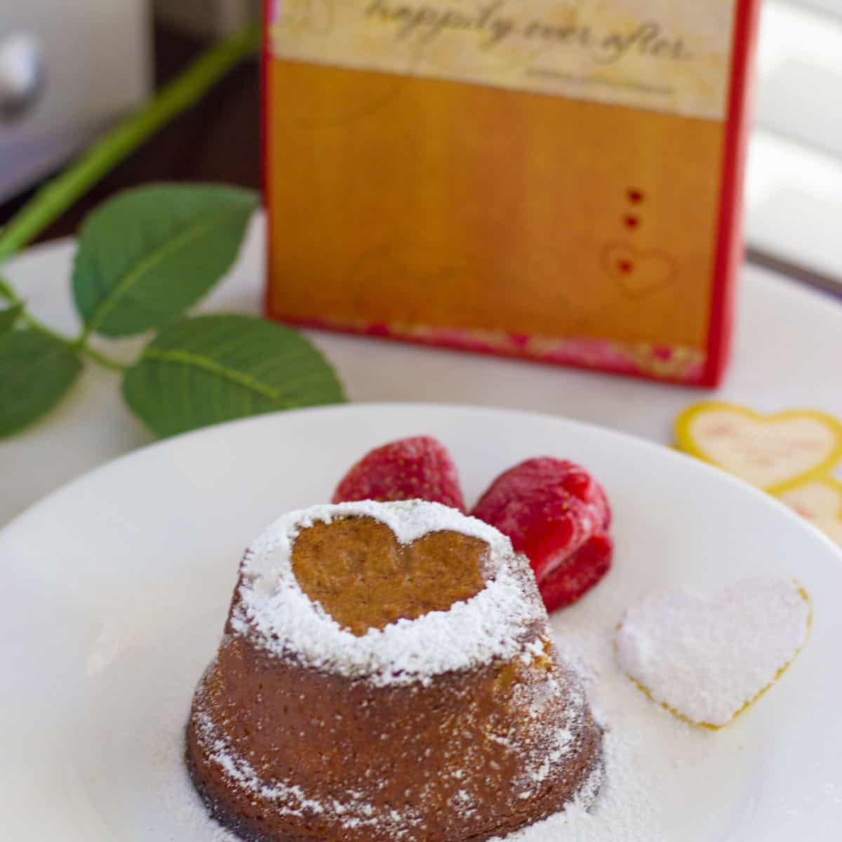 Hot choco lava cake dusted with sugar and served with strawberries on a white plate.