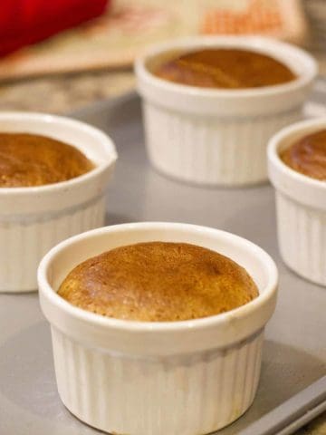 Hot choco lava cakes in four white ramekins on a gray baking tray.
