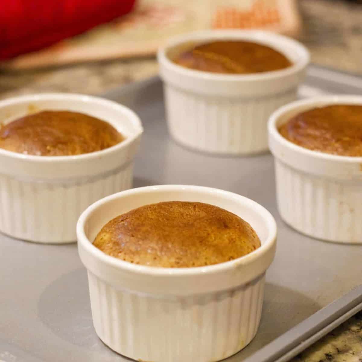 Hot choco lava cakes in four white ramekins on a gray baking tray.