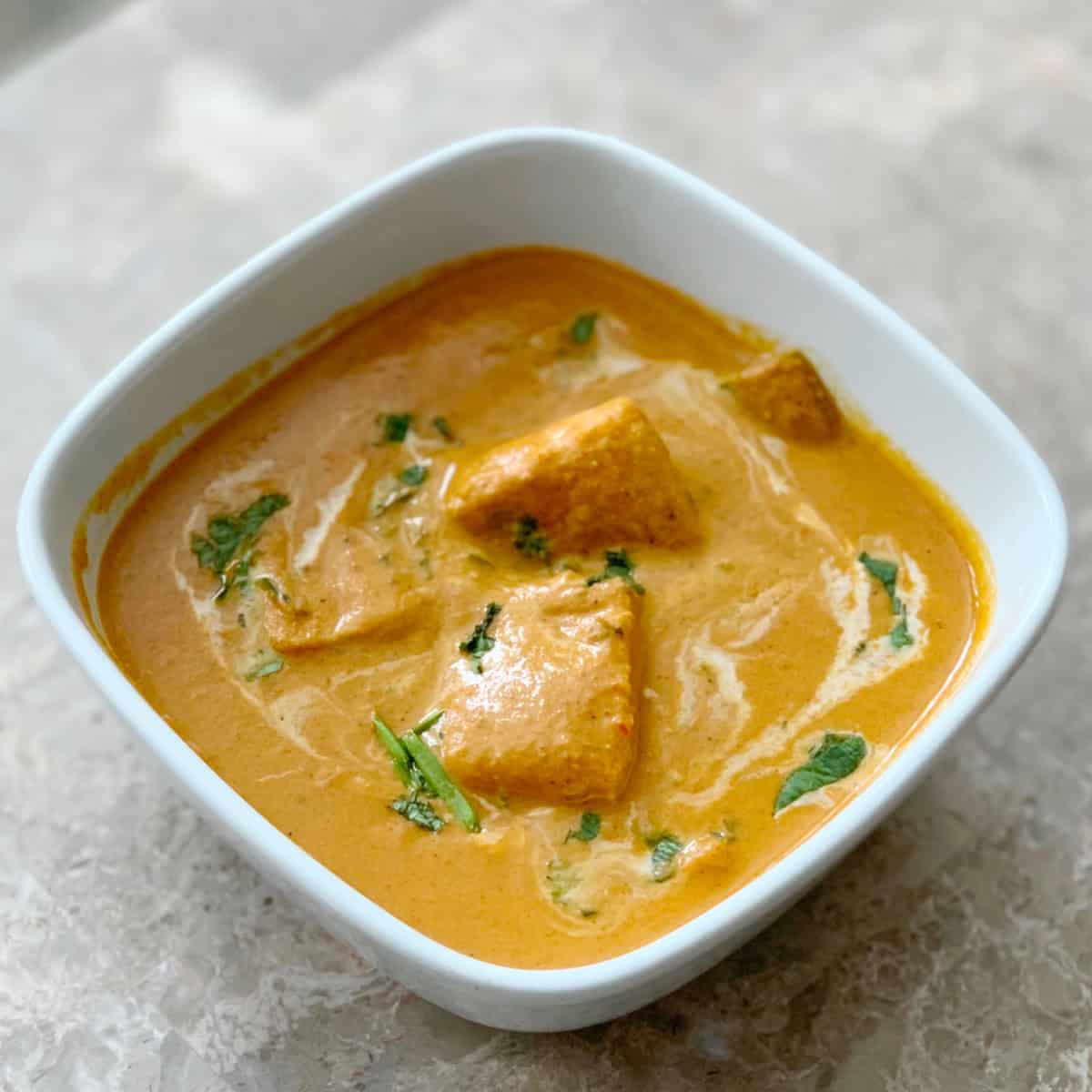 Paneer Tikka Masala Restaurant Style in a white bowl garnished with coriander leaves and cream.