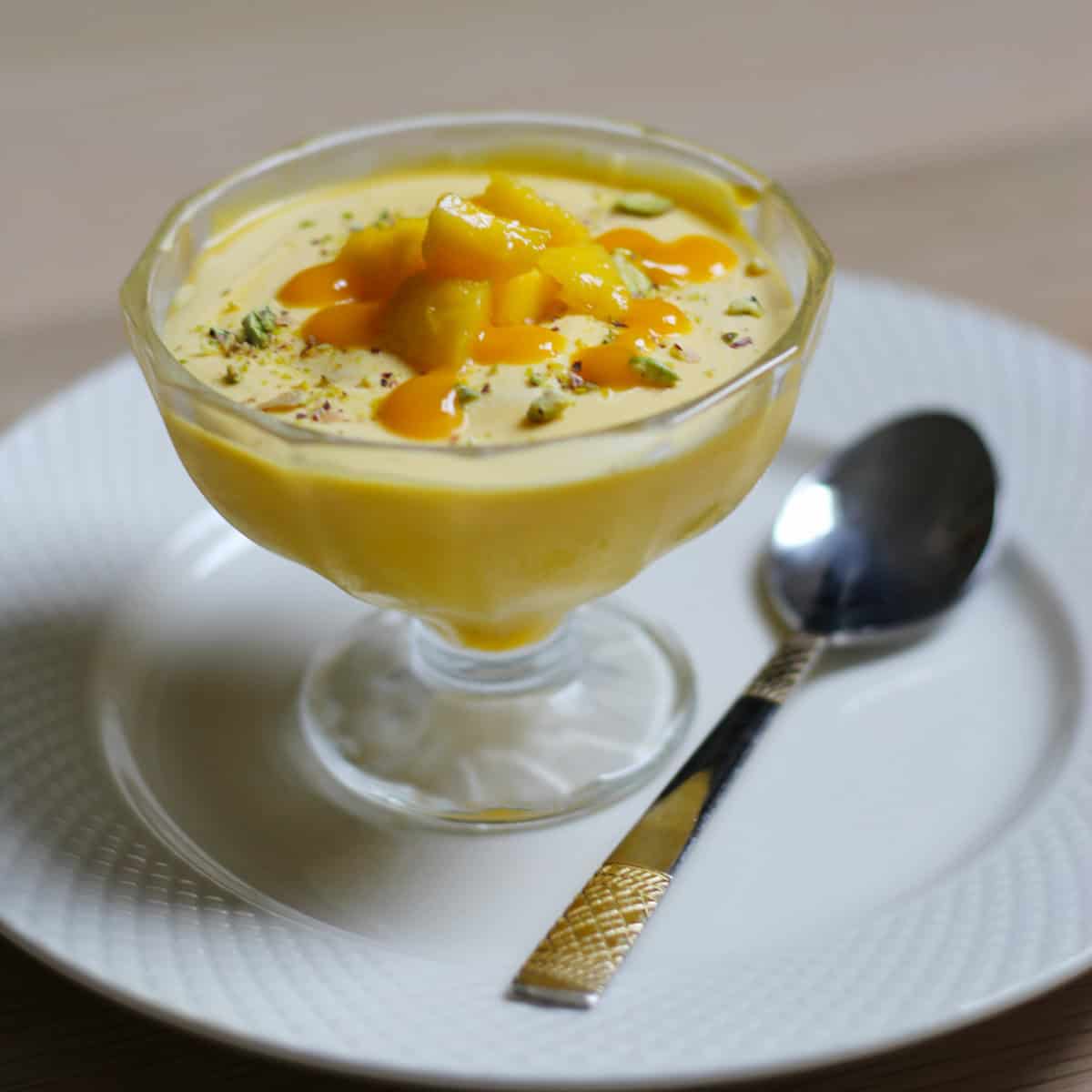 Mango mouse dessert served in dessert cup on a white plate with a spoon.