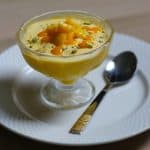 Mango mouse dessert served in dessert cup on a white plate with a spoon.