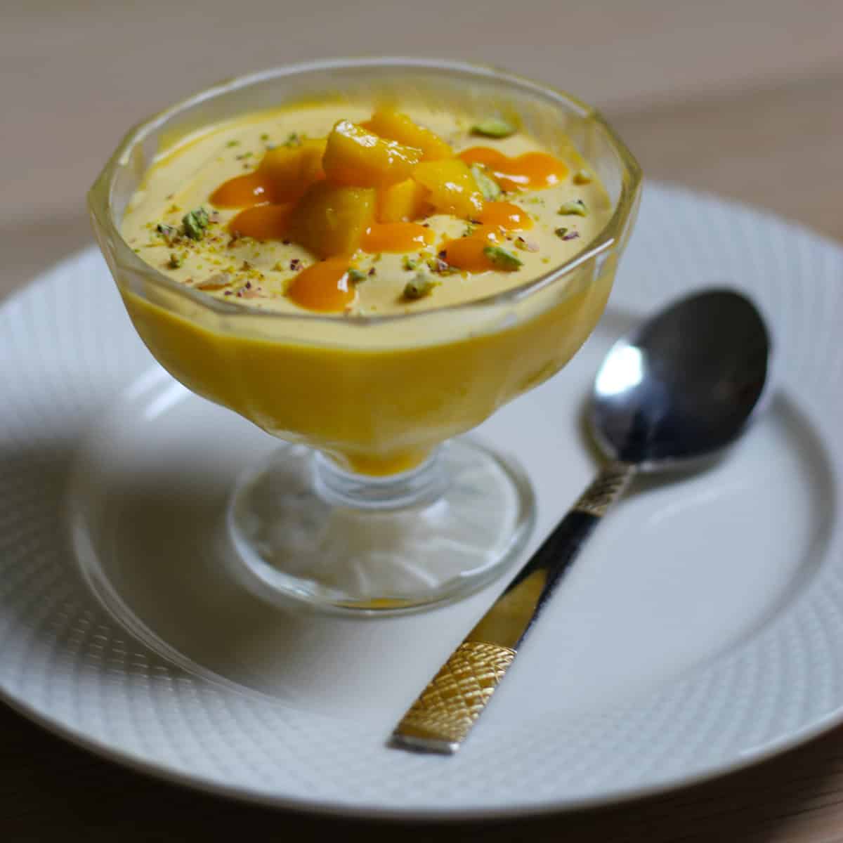 Mango mouse dessert served in dessert cup on a white plate with a spoon.