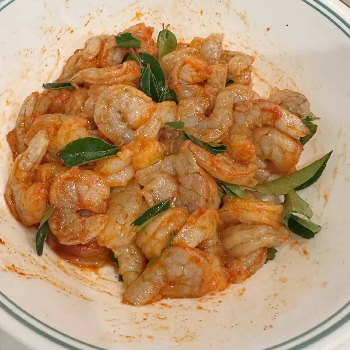 Marinating shrimp with spices and curry leaves in a white bowl to make chemmeen roast.