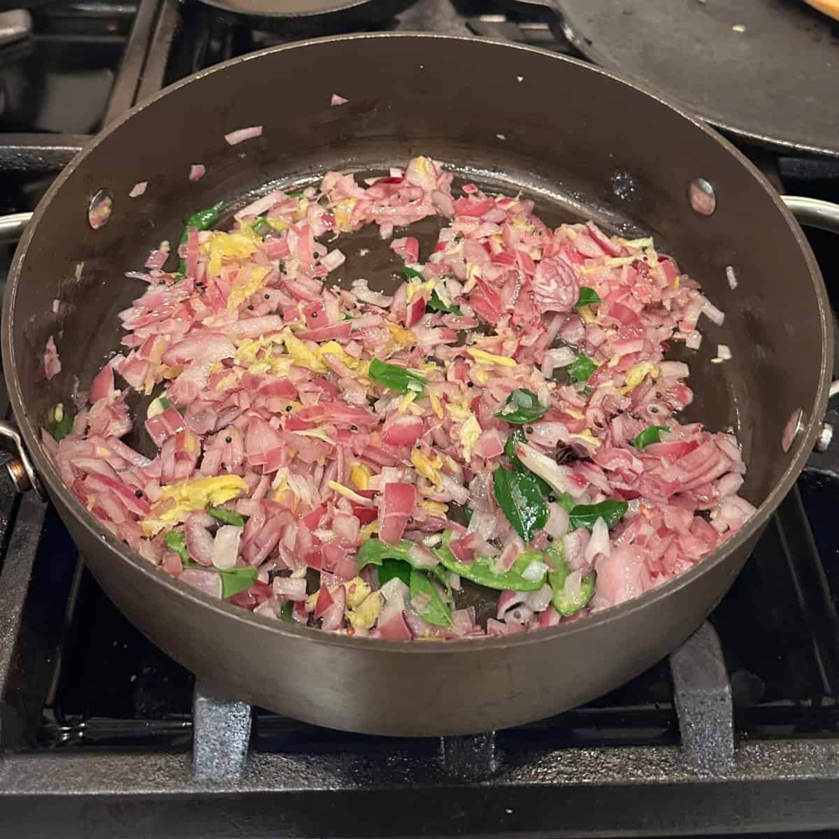 sautee onions ginger and garlic in a black pan on gas stove.