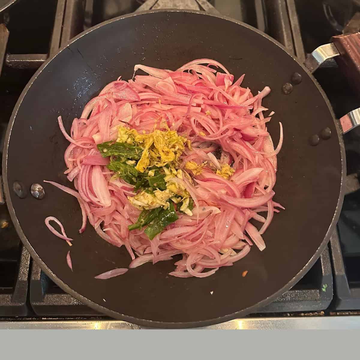 onions and ginger garlic with green chilis being sauteed in a black wok.