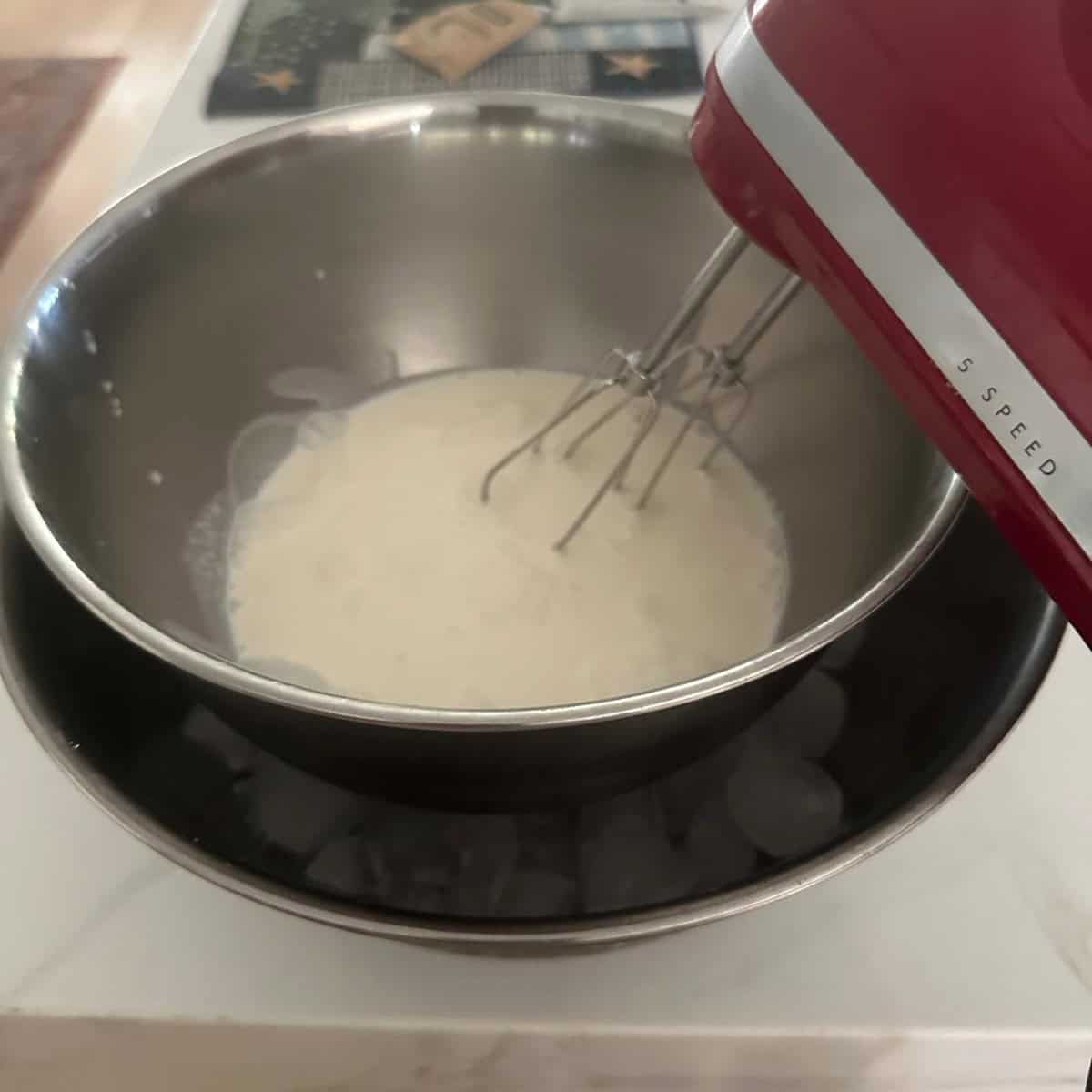 Beating whipping cream using a hand held mixer with a bowl of ice under it.