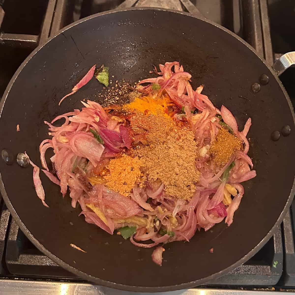Gravy prep with onions and spices for Curry chicken with coconut milk in a black wok.