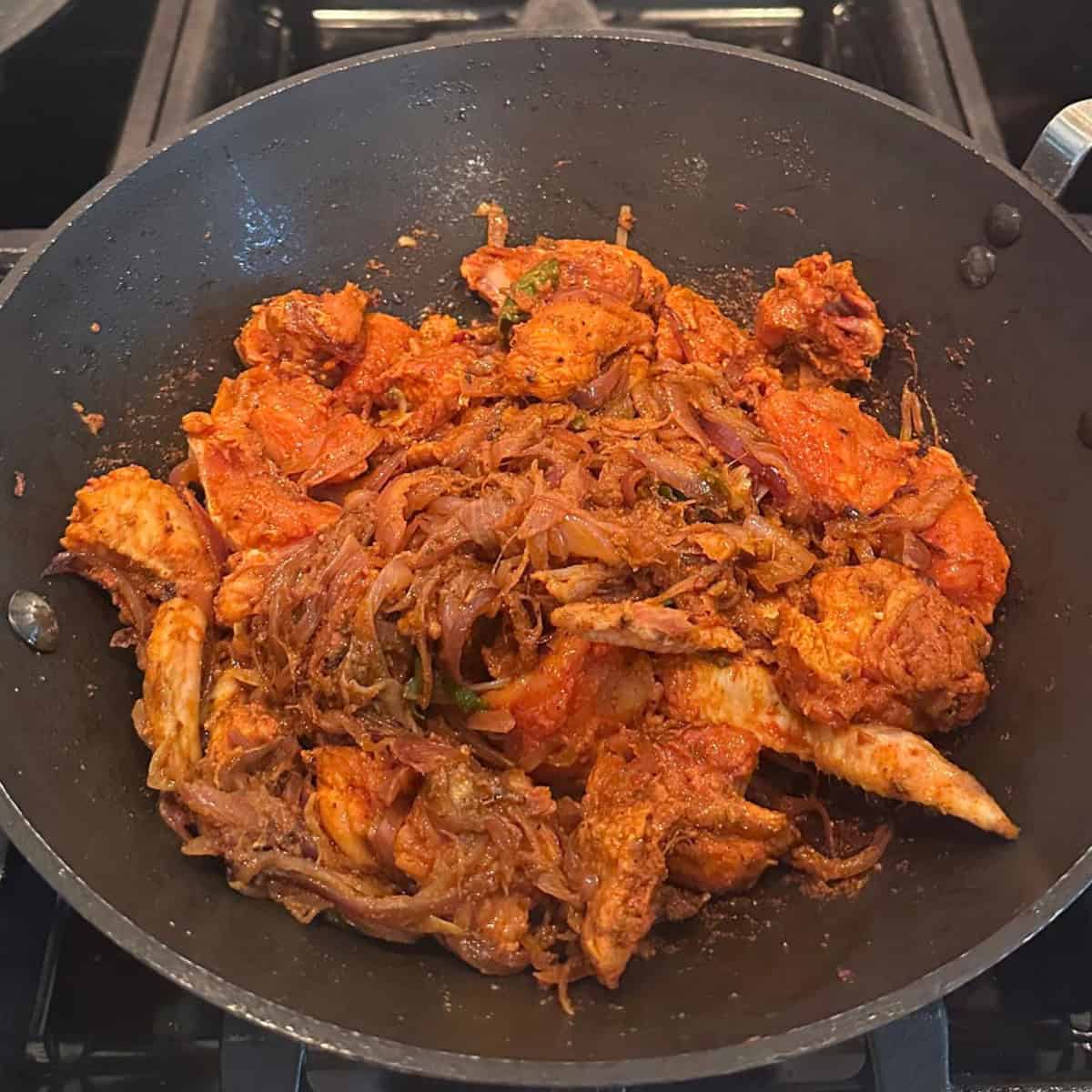 chicken added to sauteed onions in a black wok.
