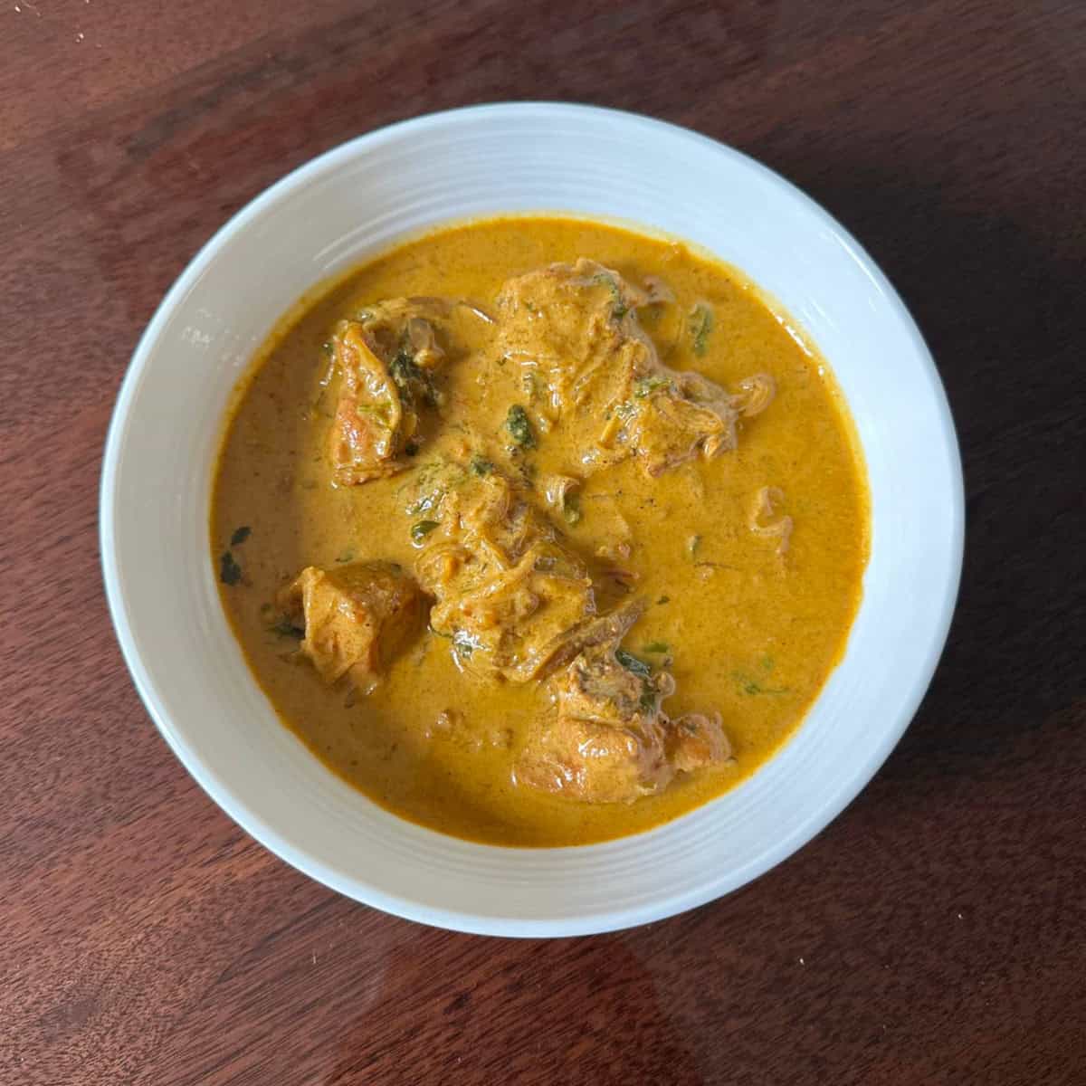 Curry chicken with coconut milk in a white bowl.
