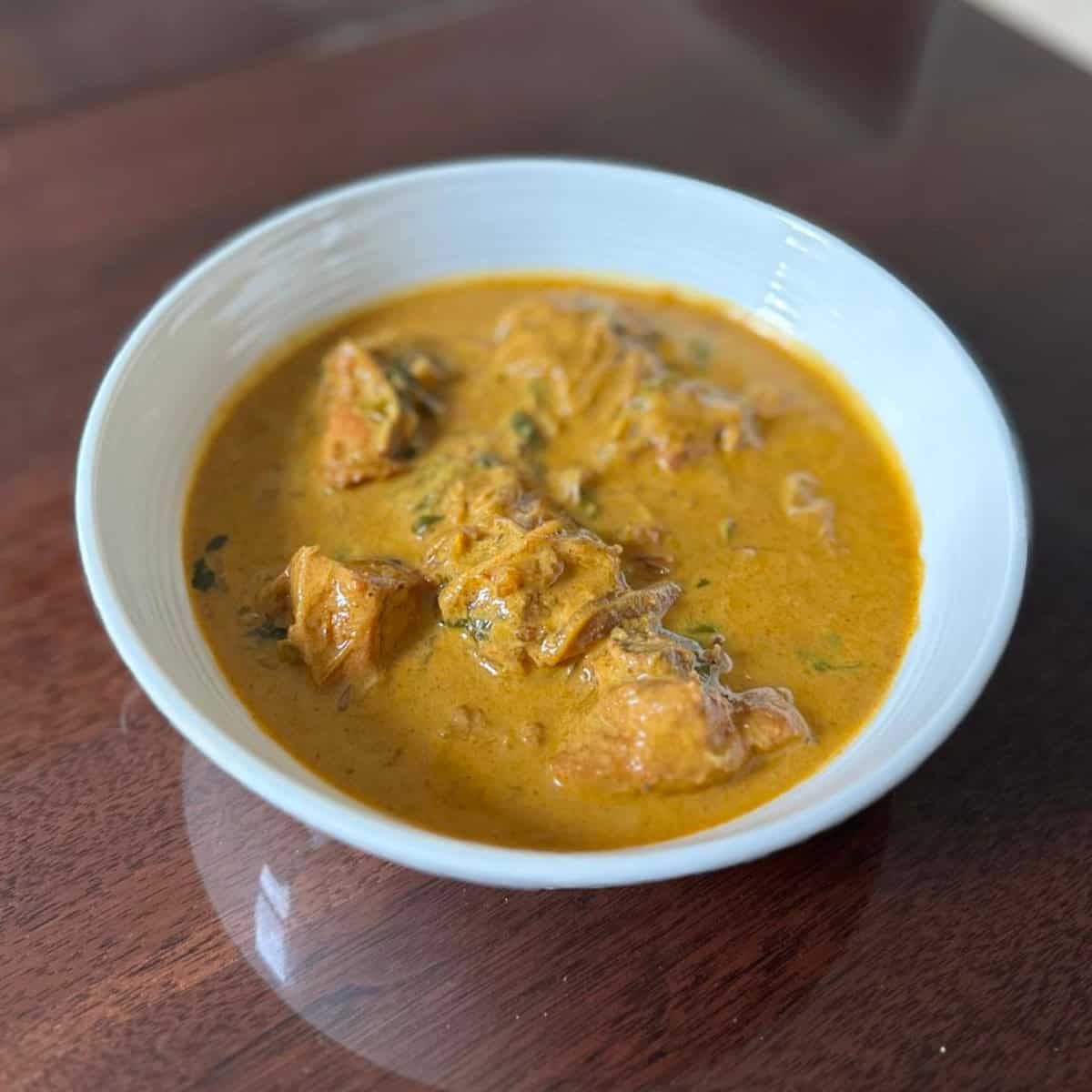 Curry chicken with coconut milk in a white bowl.