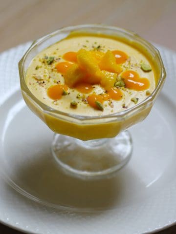 Mango mouse dessert served in dessert cup on a white plate .