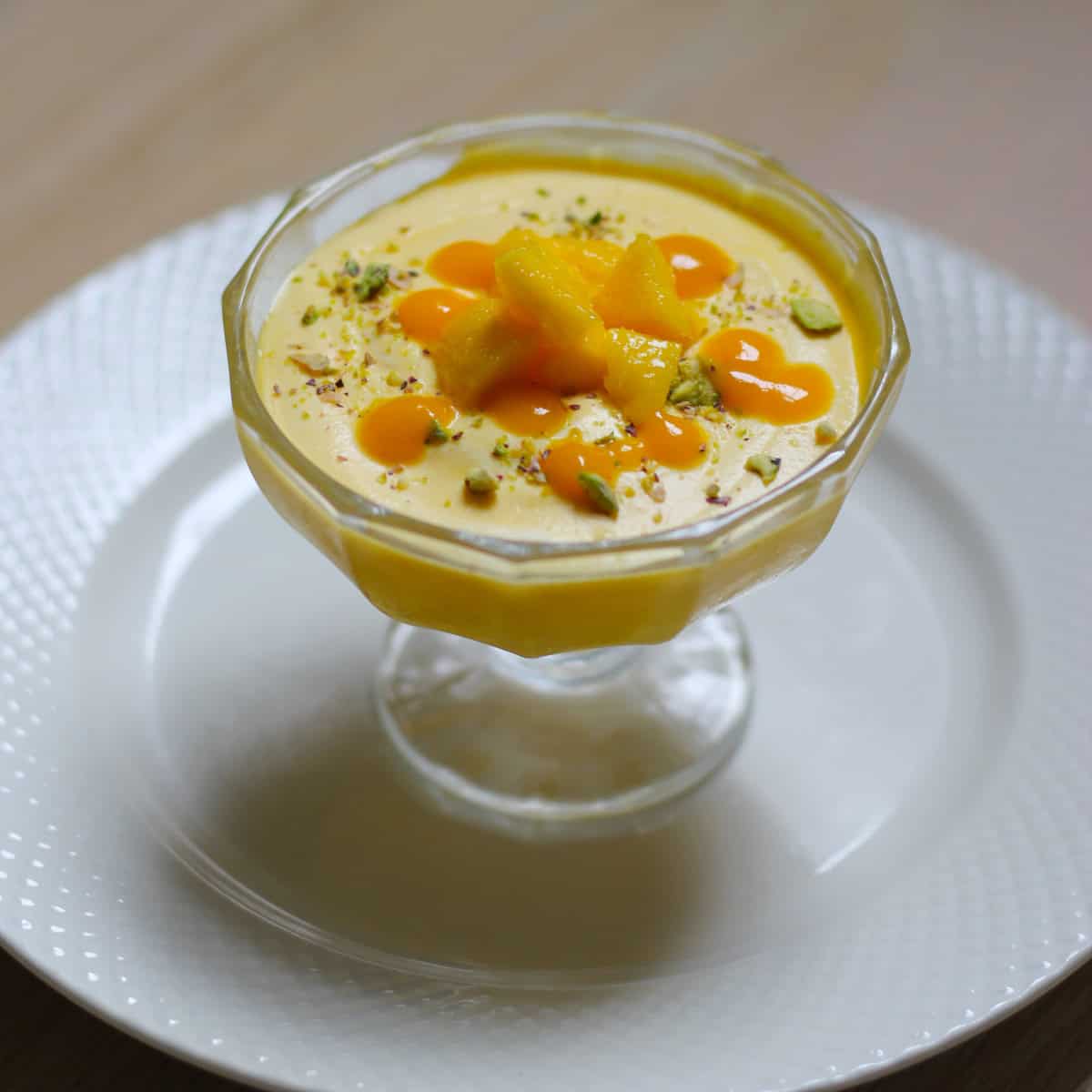 Mango mouse dessert served in dessert cup on a white plate .