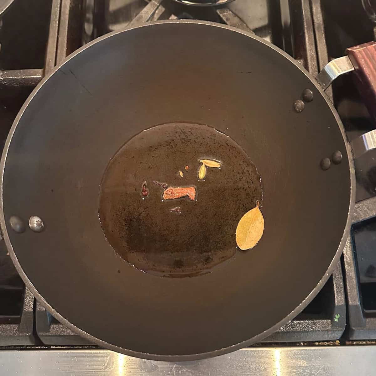 spices added to oil in a black wok.