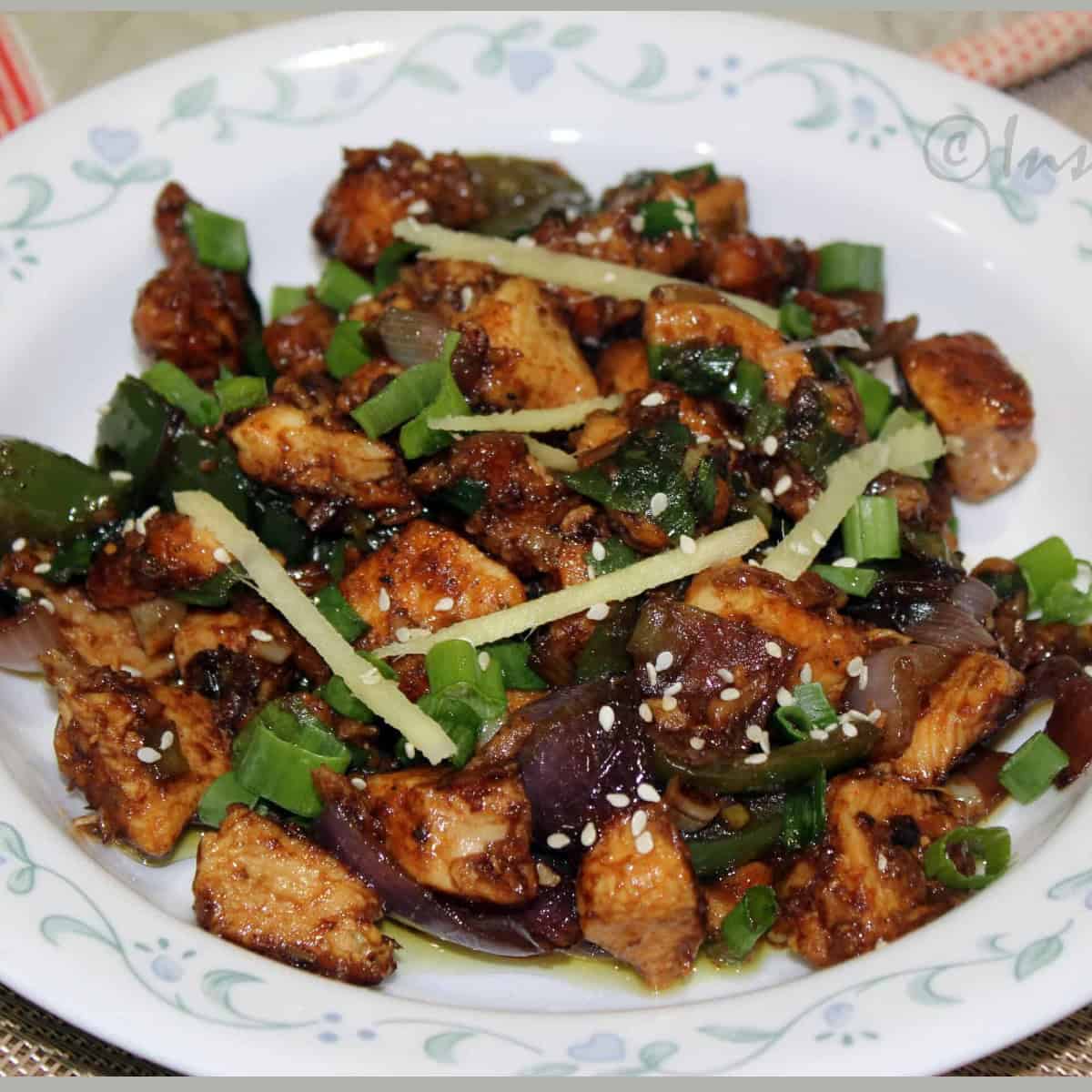 Indian Chili Chicken served in a white plate garnished with sesame and ginger.