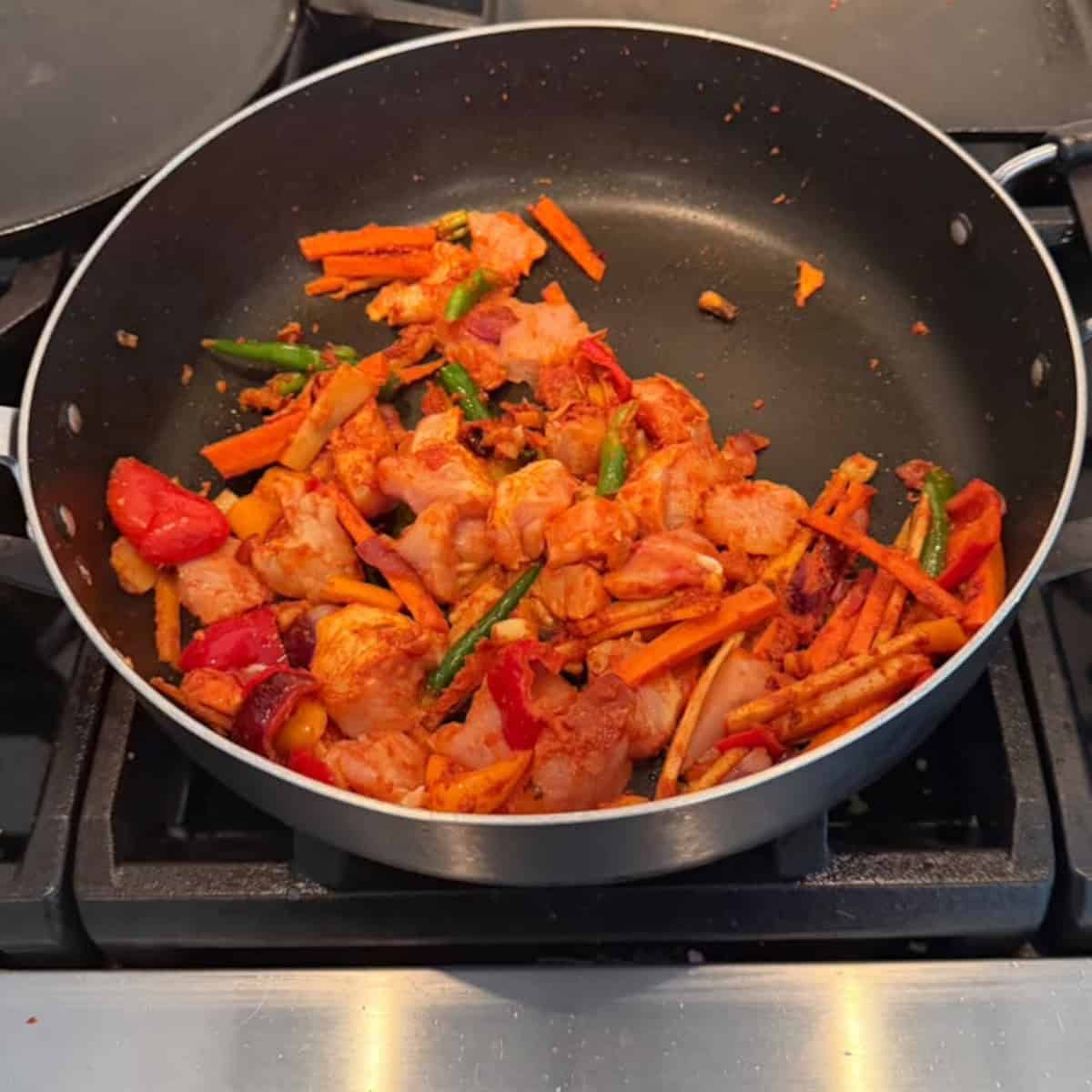 veggies with chicken sauteed in a black pan.