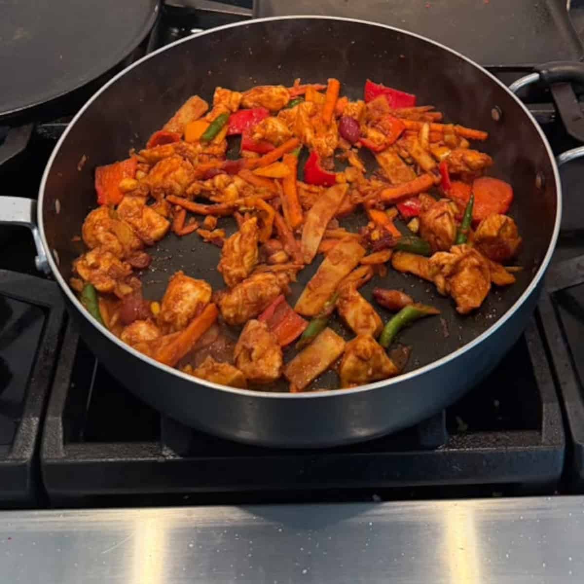 veggies with chicken sauteed in a black pan.