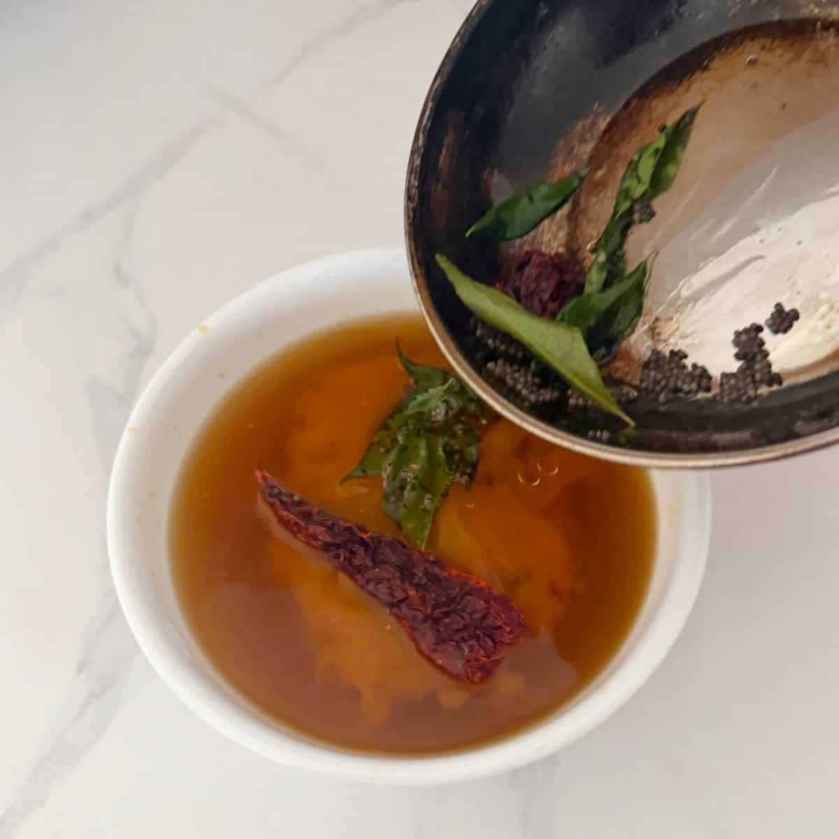 Tempering the rasam in a white bowl.